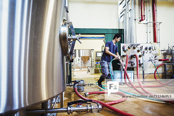 Mann  der in einer Brauerei arbeitet und Schläuche an einen metallenen Biertank anschließt.