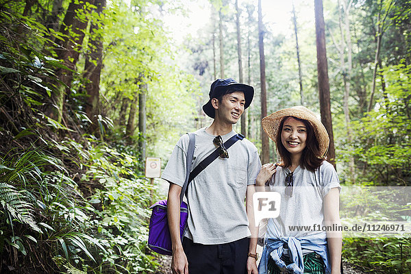 Lächelnde junge Frau und Mann stehen in einem Wald.