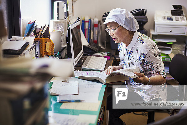 A mature woman at a desk in the office of a fast food unit and noodle production factory.