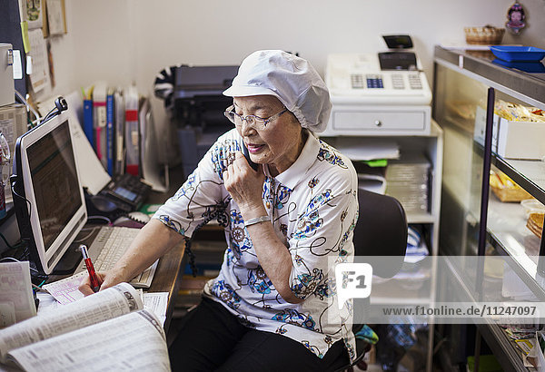 Eine reife Frau an einem Schreibtisch im Büro einer Nudelproduktionsfabrik am Telefon.