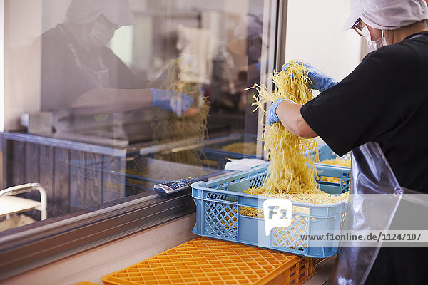 Arbeiterinnen und Arbeiter in Schürzen und Handschuhen beim Wiegen und Verpacken frisch zubereiteter Nudeln in einer Soba-Nudel-Produktionseinheit.