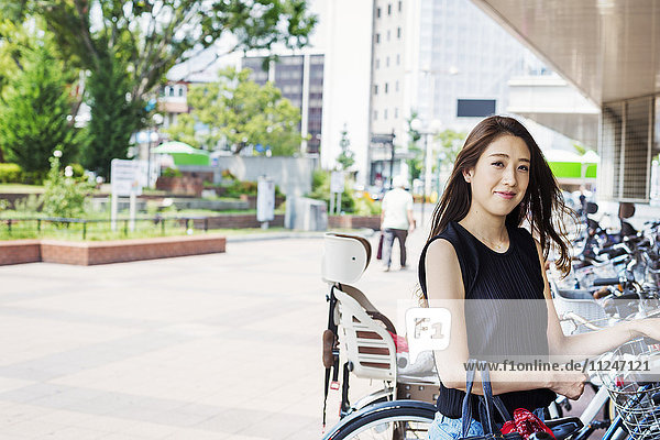 Smiling young woman with long brown hair standing next to a bicycle.