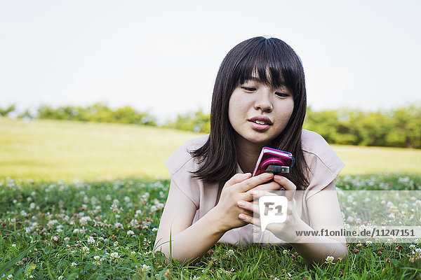 Lächelnde junge Frau mit langen braunen Haaren  die ein Mobiltelefon in der Hand hält.