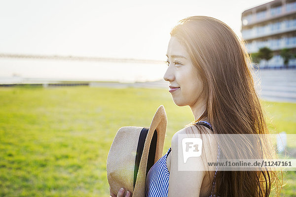 Lächelnde junge Frau mit langen braunen Haaren  Panamahut haltend.