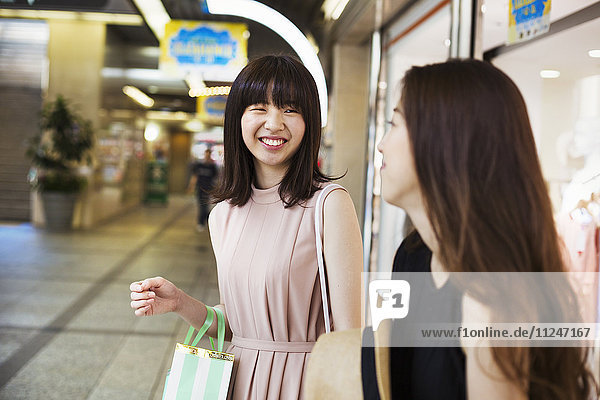 Zwei junge Frauen mit langen braunen Haaren in einem Einkaufszentrum.