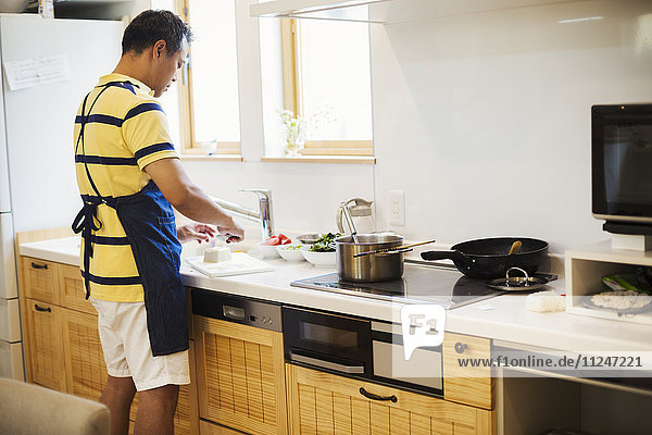 Family home. A man in a blue apron preparing a meal with his son.