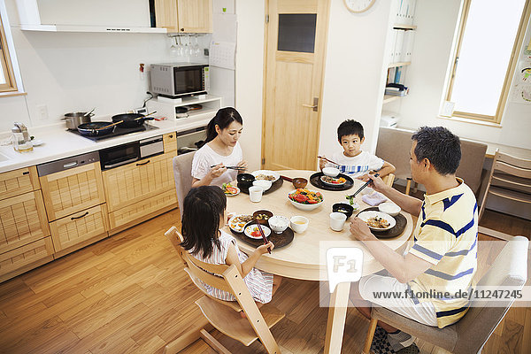 Familienhaus. Eine Familie mit zwei Erwachsenen und zwei Kindern sitzt bei einer Mahlzeit zu Hause.