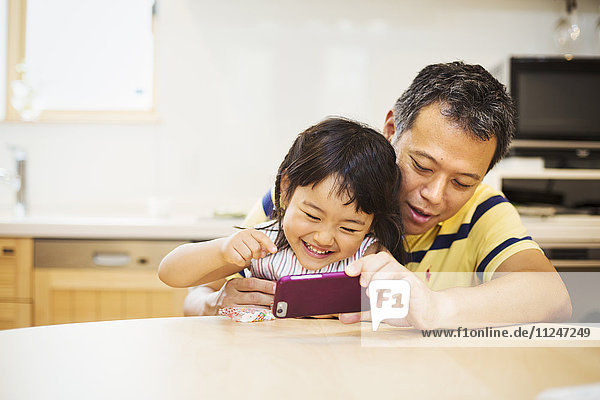 Familienhaus. Ein Mann zeigt seiner Tochter den Bildschirm eines Smartphones