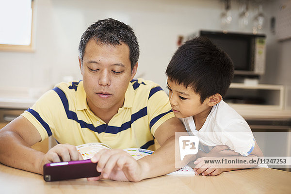 Familienhaus. Ein Mann und sein Sohn schauen auf den Bildschirm eines Smartphones.