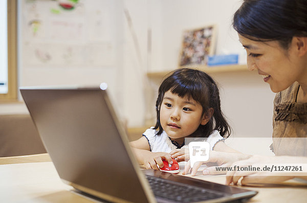 Familienhaus. Eine Frau und ihre Tochter sitzen an einem Tisch und schauen auf den Bildschirm eines Laptops.