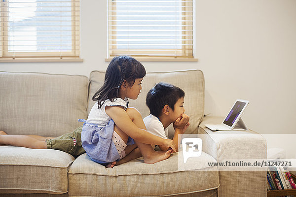 Family home. A boy and a girl lying on a sofa watching a digital tablet.
