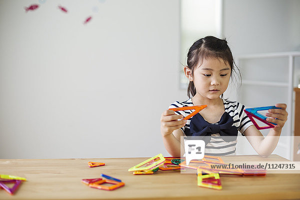 Ein Mädchen sitzt und spielt mit farbigen geometrischen Formen.