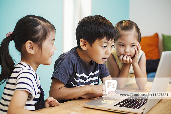 Drei Kinder mit einem Laptop  zwei Mädchen und ein Junge.