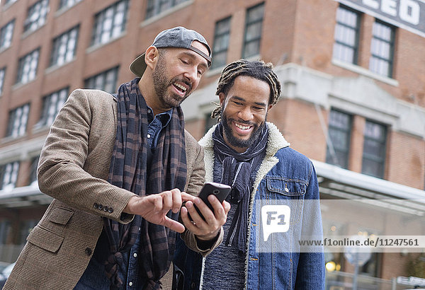 Smiley homosexuelles Paar schaut auf Smartphone auf der Straße