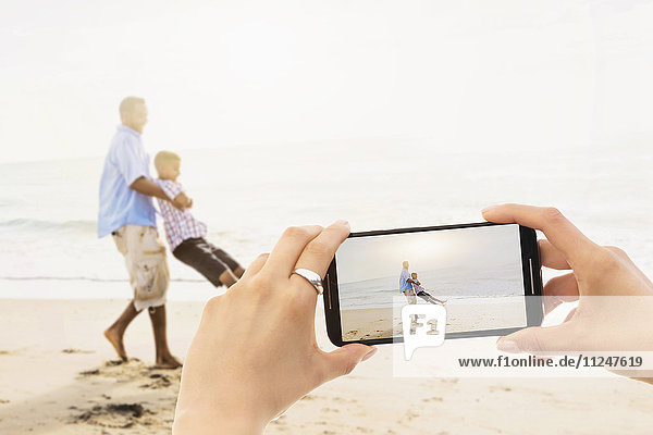 Persönliche Perspektive einer Frau  die ihren Vater beim Spielen mit ihrem Sohn (12-13) am Strand fotografiert