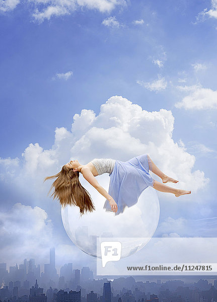 Junge Frau schwebt auf einer Seifenblase über einer Stadtlandschaft