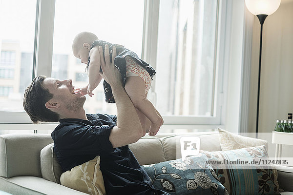 Vater sitzt auf dem Sofa und spielt mit seiner kleinen Tochter (2-5 Monate)