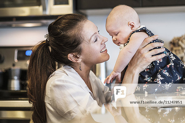 Mother playing with baby daughter (2-5 months) in kitchen