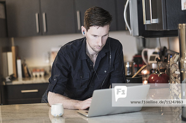 Mann arbeitet in der Küche an einem Laptop-Computer