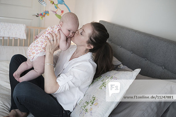 Mother kissing baby daughter (2-5 months) in bedroom