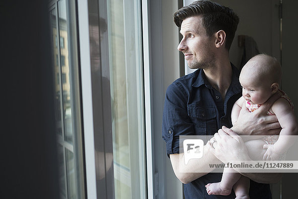 Vater schaut mit Tochter durch das Fenster (2-5 Monate)
