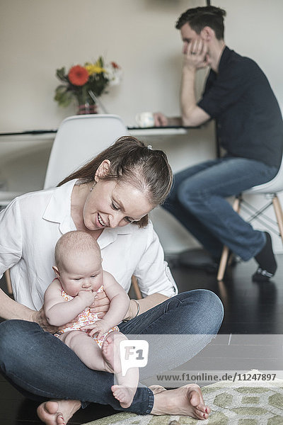 Mother holding baby (2-5 months) and father working in background