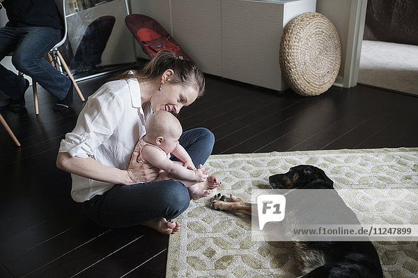 Mutter hält Baby (2-5 Monate) und spielt mit Hund