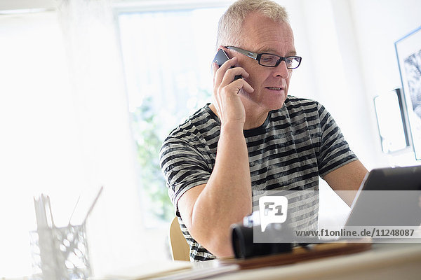Man in home office using smartphone and tablet