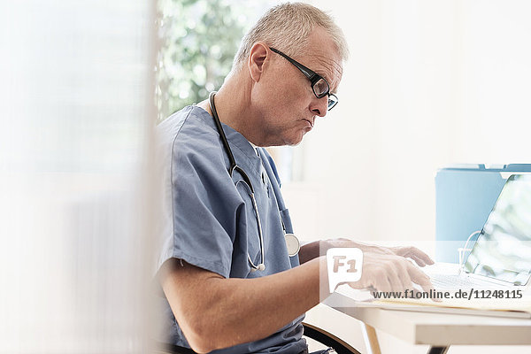 Mann im Kittel benutzt Laptop in einer Arztpraxis