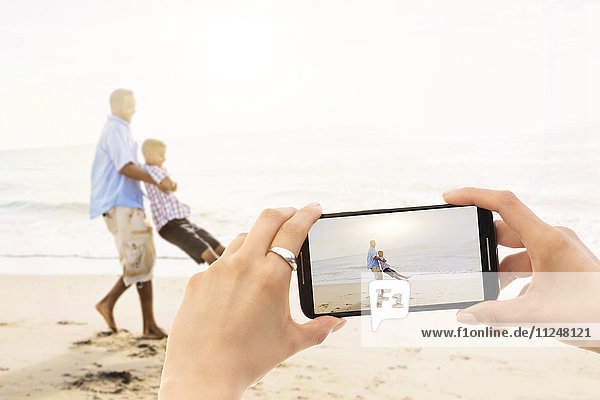 Junge Frau fotografiert Vater mit Sohn (12-13) am Strand