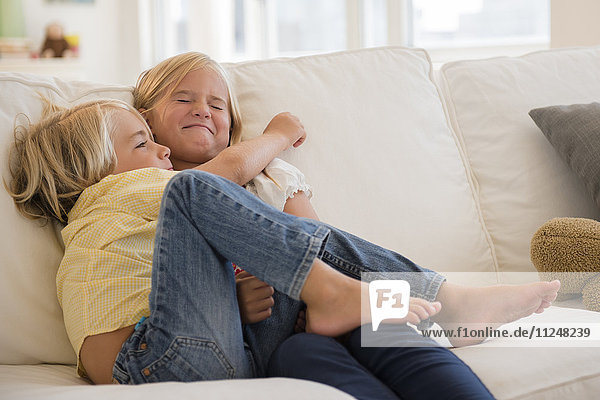 Boy (4-5) and girl (6-7) hugging on sofa