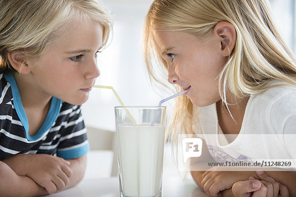 Bruder (4-5) mit Schwester (6-7)  die Milch aus einem Glas trinken
