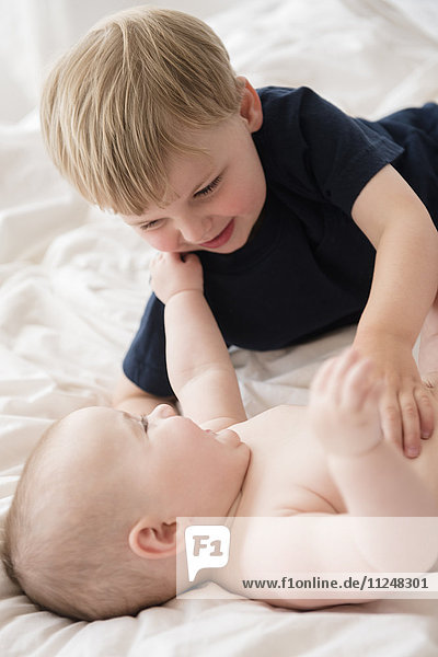 Bruder (2-3) spielt mit kleiner Schwester (12-17 Monate) im Bett