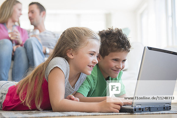 Boy and girl (6-7  8-9) lying on floor and using laptop