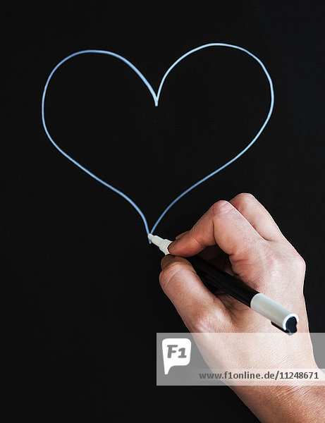 Man's hand drawing heart shape on black paper