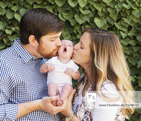 Happy parents kissing girl (2-5 months)