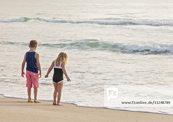 Junge (6-7) und Mädchen (4-5) stehen am Strand am Wasser