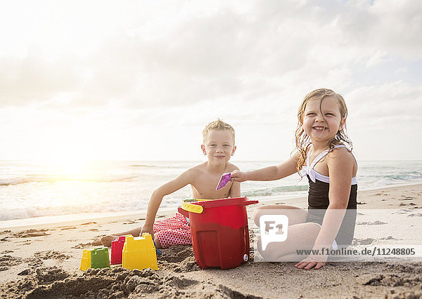 Junge (6-7) und Mädchen (4-5) spielen mit Sand am Strand