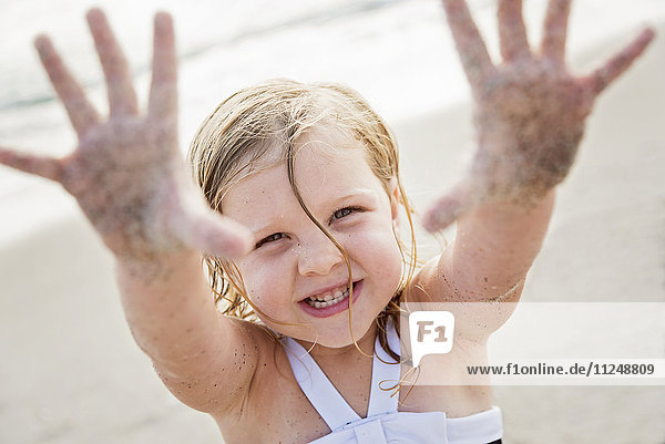 Mädchen (4-5) am Strand zeigt ihre schmutzigen Hände