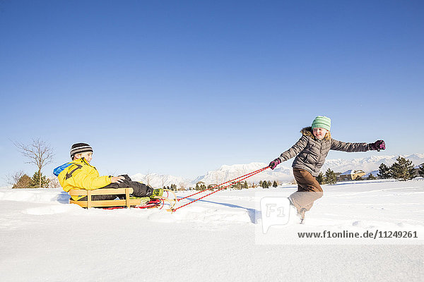 Children (8-9) playing with sled in snow