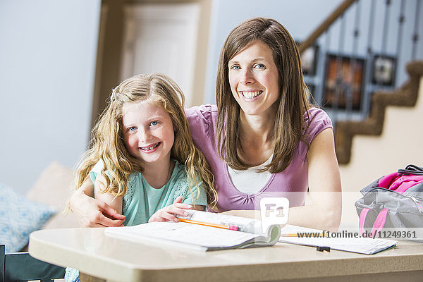 Lächelnde Mutter und Tochter (8-9) sitzen am Tisch und lernen