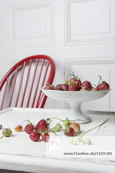 Erdbeeren in Porzellanschale auf Holztisch  im Hintergrund weisse Holztüre und roter Holzstuhl