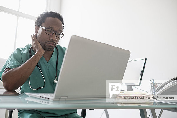 Männlicher Arzt arbeitet mit Laptop am Schreibtisch