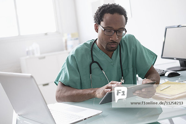 Männlicher Arzt arbeitet mit digitalem Tablet am Schreibtisch