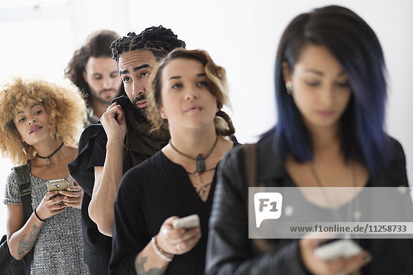 Junge Menschen  die mit ihren Smartphones in der Schlange stehen