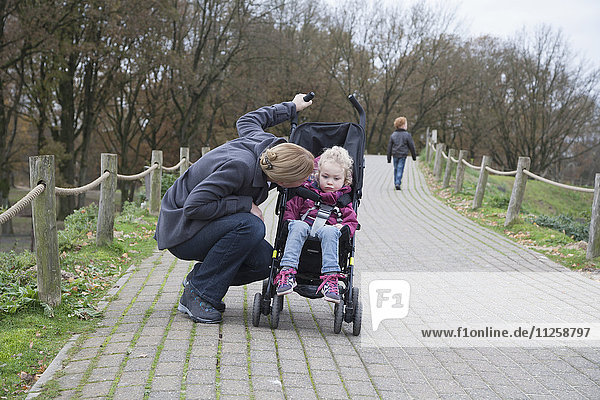 Mother talking to daughter (4-5) sitting in stroller  boy (8-9) walking in background