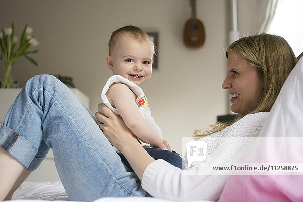 Mother and daughter (18-23 months) sitting on bed and smiling