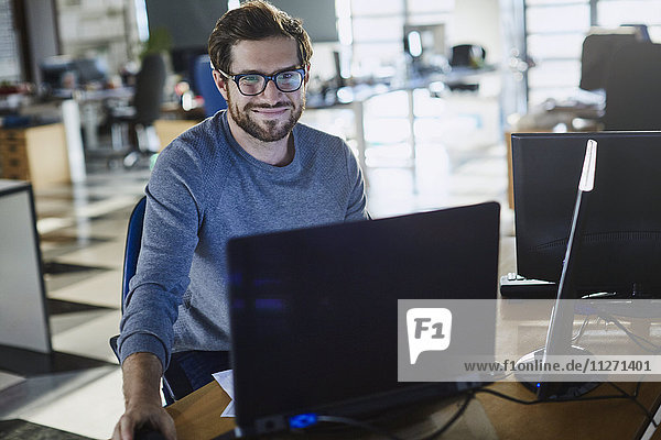 Porträt eines lächelnden Geschäftsmannes  der am Computer im Büro arbeitet