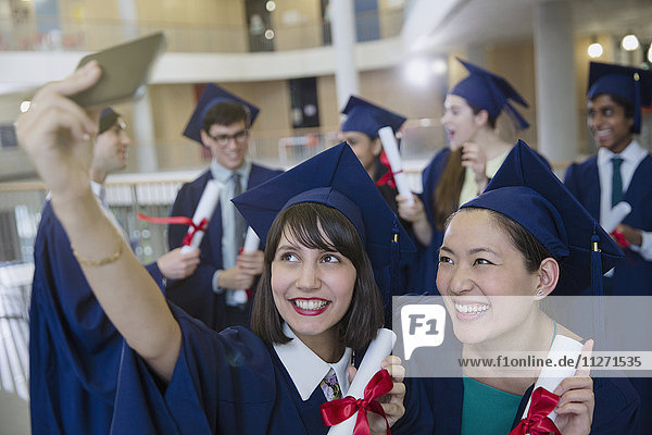 College women graduates in cap and gown taking selfie with diplomas