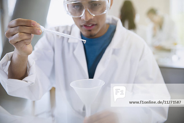 Male college student conducting scientific experiment using pipette in science laboratory classroom